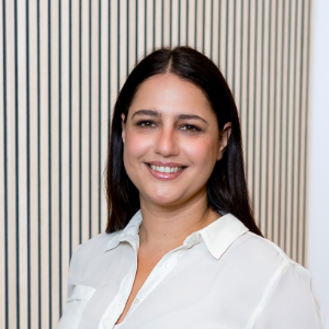 Eine Frau mit langen dunklen Haaren und einer weißen Bluse lächelt in die Kamera.