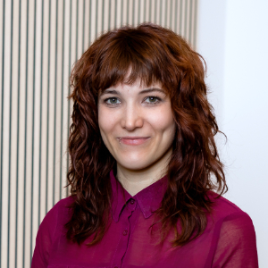 Eine Frau mit rotbraunem, schulterlangem Haar lächelt in magentafarbenem Hemd in die Kamera.