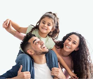 Ein lächelnder Mann trägt ein junges Mädchen Huckepack, während eine Frau neben ihnen steht. Alle drei sehen glücklich aus und verkörpern vor einem schlichten hellen Hintergrund Teilhabe und Freude.